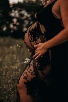 a pregnant woman standing in a field with her hands on her stomach, wearing a sheer black dress