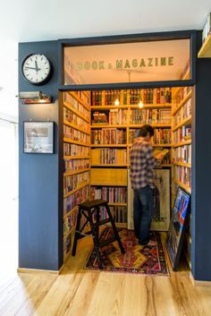 a man standing in front of a bookshelf filled with lots of books next to a clock