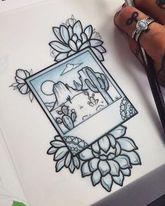 a drawing of a cactus in a frame with mountains and flowers on it next to a person's hand