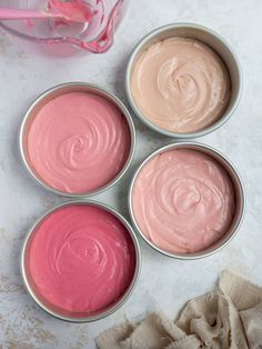 four tins filled with pink and white icing sitting on top of a table