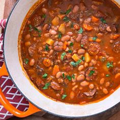 a large pot filled with beans and meat on top of a wooden table next to a red towel