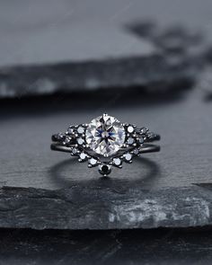 a white diamond ring sitting on top of a black stone slab, with the center surrounded by smaller round diamonds