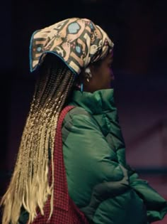 a woman with long braids wearing a green jacket and a white hat on top of her head