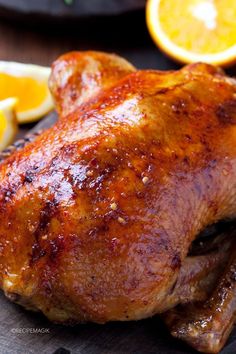 a close up of a chicken on a cutting board with lemons and an orange in the background