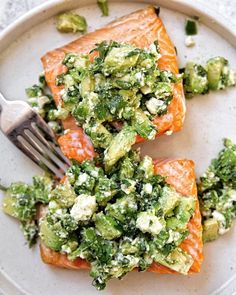 two pieces of salmon on a plate with broccoli and other toppings next to a fork