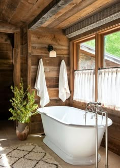 a white bath tub sitting in a bathroom next to a window with curtains on it