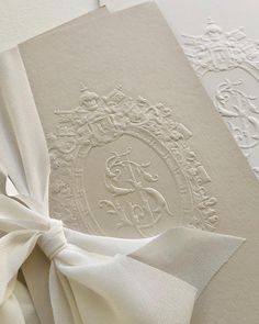 a white wedding card with a bow on the front and back, decorated with an ornate monogram