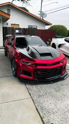 a red chevrolet camaro parked in front of a house