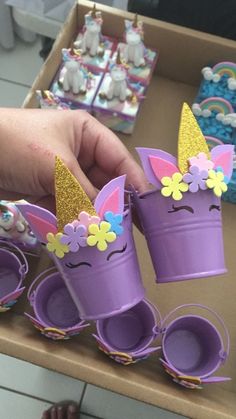 a person is holding some purple cups with unicorns on them in front of other cupcakes