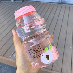 a person holding a plastic bottle with peach milk in it