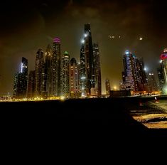 the city skyline is lit up at night with bright lights in the sky and clouds