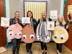 three women holding up paper cutouts with faces on them