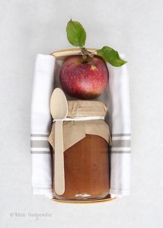 an apple sitting on top of a wooden spoon next to a jar of peanut butter