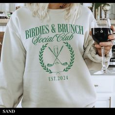 a woman holding a glass of wine in her right hand and wearing a sweatshirt with the words bridals & brunch social club on it