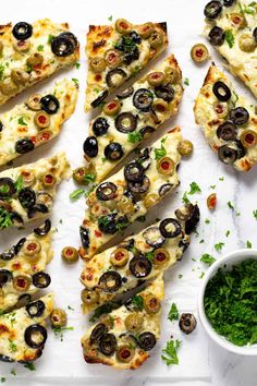 several slices of pizza with olives and parsley next to a small bowl of pesto