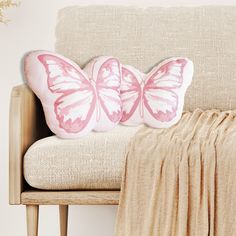 two pink butterfly pillows sitting on top of a beige couch next to a tan blanket