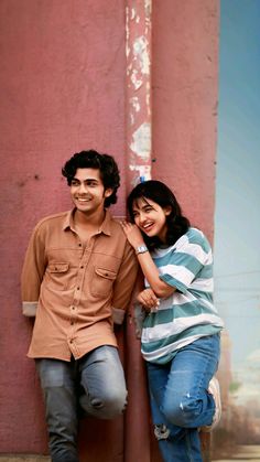 a man and woman are leaning against a wall smiling at the camera with their arms around each other