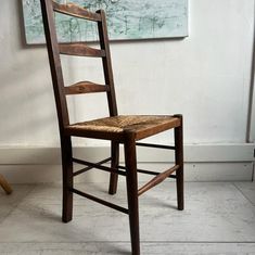 a wooden chair sitting in front of a painting on the wall next to a floor