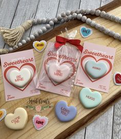 some heart shaped cookies are on a wooden tray with cards and beads next to them