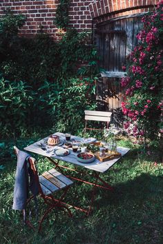 an outdoor table with food on it in front of a brick building and flowers growing around