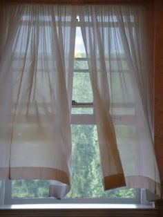 a window with white curtains in front of it and trees outside the window sill