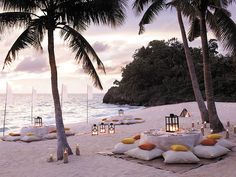 an outdoor dining area on the beach with candles and lanterns lit up in front of the ocean