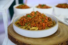 a white bowl filled with pasta and meat on top of a wooden table next to bowls of sauce