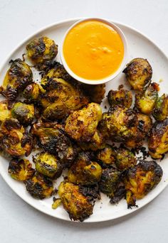 a white plate topped with roasted brussel sprouts next to a bowl of orange sauce