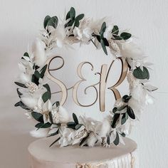 a wedding cake with white flowers and greenery on the top is decorated with a wooden monogram