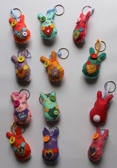 several small stuffed animals are hanging from key chains on a white surface, with buttons in the shape of an animal's head