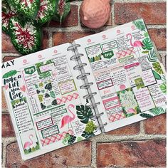 an open planner book sitting on top of a brick wall next to potted plants