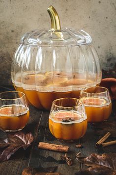 three glasses filled with liquid sitting on top of a wooden table next to a pumpkin