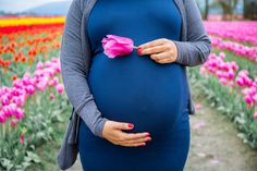 a pregnant woman holding a pink flower in front of a field of tulips