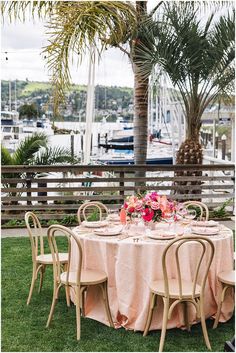 an outdoor table set up with pink linens and flowers for a wedding reception at the marina