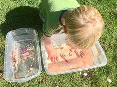 a little boy playing with some food on the grass in front of two plastic containers