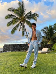 a man standing on top of a lush green field next to a palm tree with his shirt off