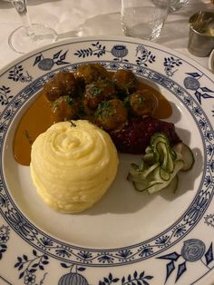 a plate with meatballs, mashed potatoes and cucumbers on it sits on a table