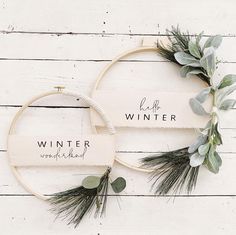 two hoop wreaths decorated with greenery and the words winter on them, sitting next to each other