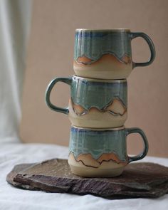 three coffee mugs stacked on top of each other in the shape of mountains and clouds