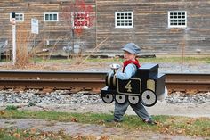 a young boy dressed as a train conductor carrying a box with the number four on it