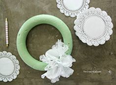 doily and paper flowers are laid out on the table to make a wreath decoration