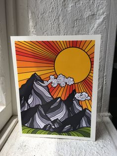 a card with an image of mountains and clouds in the background, on a window sill