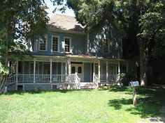 a large blue house sitting in the middle of a lush green field with lots of trees