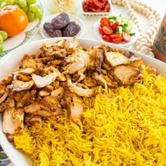 a white plate topped with rice covered in meat and veggies next to other foods