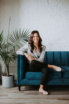 a woman sitting on a blue couch in front of a potted plant and smiling