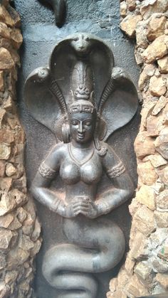 an ancient statue in the shape of a woman with her hands on her hips, sitting against a stone wall