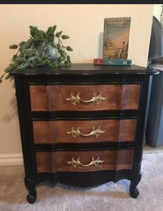 a black and brown chest of drawers with gold hardware on the handles, in front of a white wall