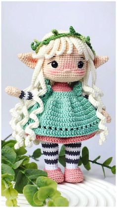 a crocheted doll is standing next to some leaves