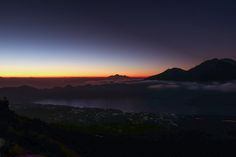 the sun is setting over some mountains with clouds in the foreground and fog on the ground