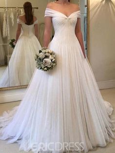 a woman standing in front of a mirror wearing a wedding dress with off the shoulder sleeves